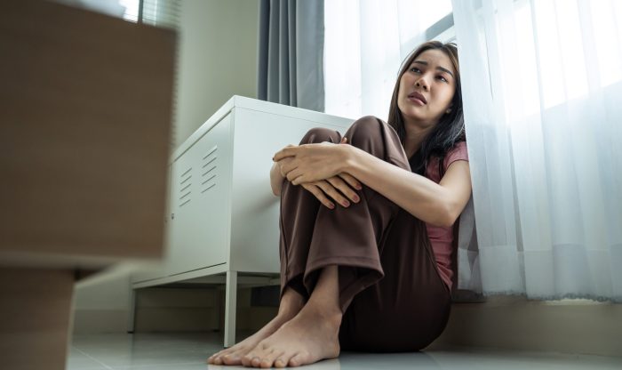 Asian young upset depressed woman sitting alone in living room at home. Attractive unhappy female feeling very sad, lonely and frustrated with life problem think of money debt, budget loss, bankruptcy
